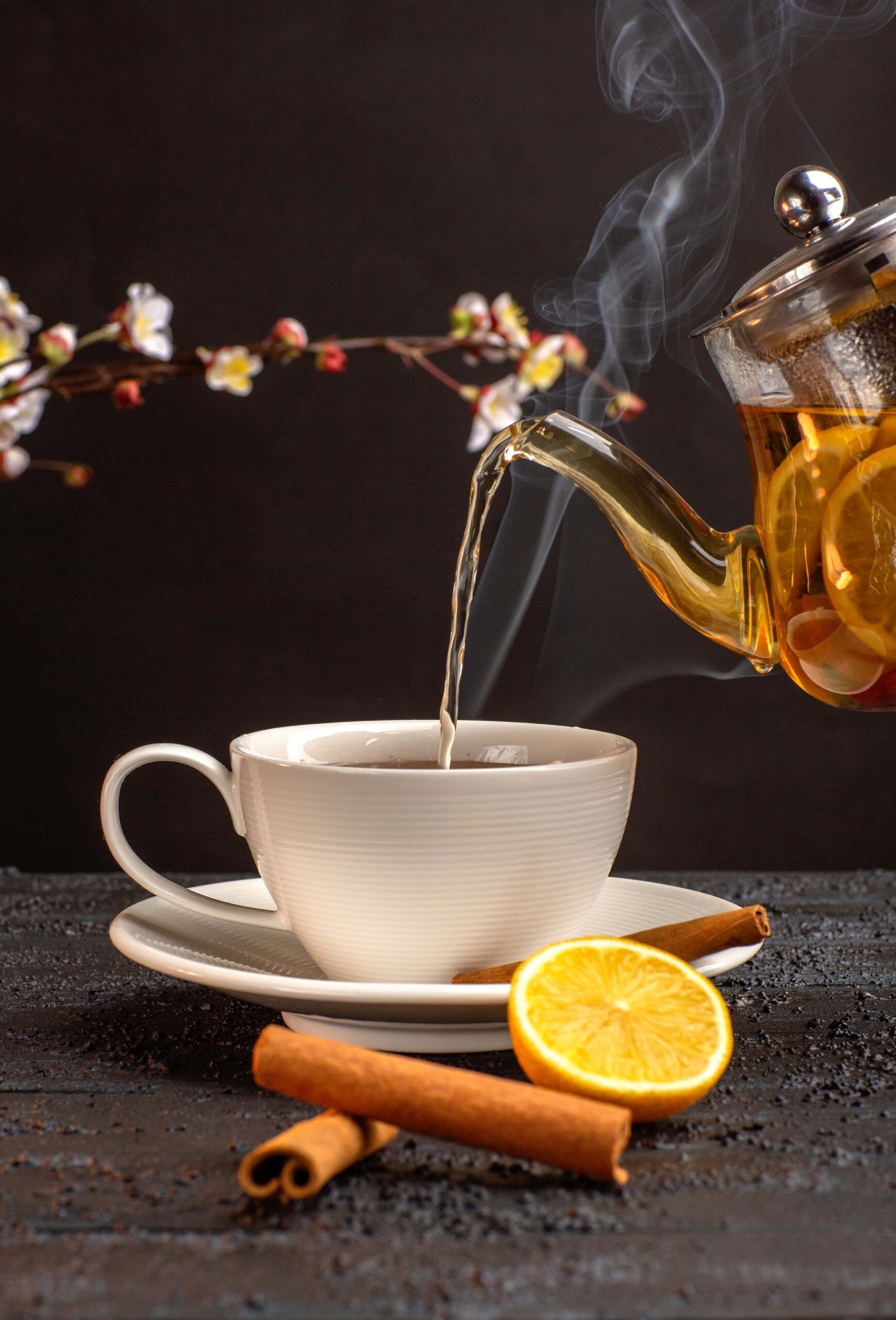 front view cup of tea with lemon cinnamon and kettle on grey des